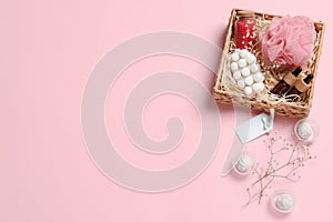 Spa gift set of different luxury products in wicker basket on pale pink background, flat lay. Space for text