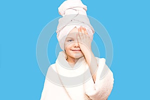 Spa girl. Beautiful blue-eyed child girl in white robe and towel on her head after bath touch face. Perfect Skin. Skincare