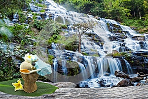 Spa herbal compressing ball,white frangipani flower,turmeric powder in white spoon massage oil in bamboo basket at waterfall