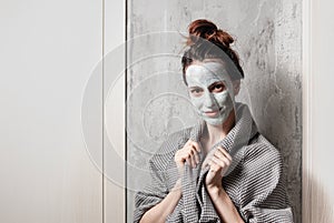 Spa at home, a girl in a gray bathrobe makes a face mask at home on a background of gray-beige wall photo