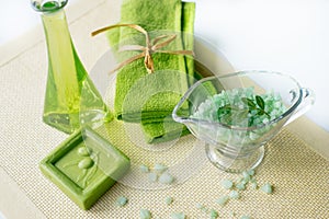 Spa kit: liquid soap, sea salt, green towel, fresh flowers, olive leaves on an old yellow napkin on a white background