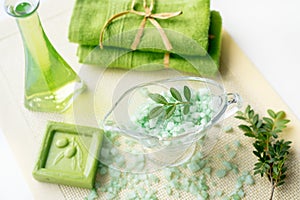 Spa kit: liquid soap, sea salt, green towel, fresh flowers, olive leaves on an old yellow napkin on a white background