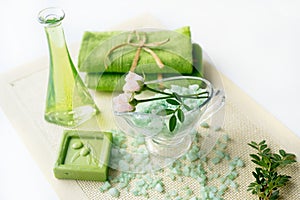 Spa kit: liquid soap, sea salt, green towel, fresh flowers, olive leaves on an old yellow napkin on a white background