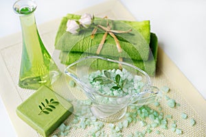 Spa kit: liquid soap, sea salt, green towel, fresh flowers, olive leaves on an old yellow napkin on a white background