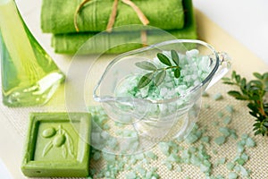 Spa kit: liquid soap, sea salt, green towel, fresh flowers, olive leaves on an old yellow napkin on a white background