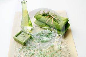 Spa kit: liquid soap, sea salt, green towel, fresh flowers, olive leaves on an old yellow napkin on a white background