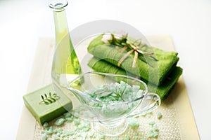 Spa kit: liquid soap, sea salt, green towel, fresh flowers, olive leaves on an old yellow napkin on a white background