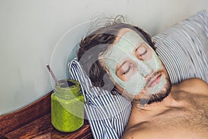 Spa man applying Facial green clay Mask. Beauty Treatments. Fresh green smoothie with banana and spinach with heart of sesame see