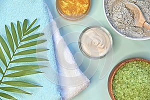 Spa massage clay powder, face masks, bath salt, towel, shea butter on blue table background.