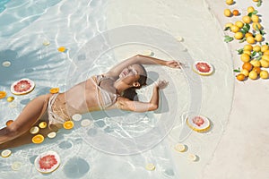 SPA Model In Pool With Citrus. Beautiful Girl In Bikini Floating With Fresh Tropical Fruit At Resort.