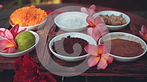 Spa powders in small bowls on wooden table with frangipani