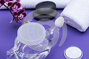 Spa purple background with Neti Pot, pile of Saline, rolled up White Towels, stacked Basalt Stones and Orchid Flower. Sinus wash.