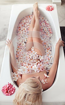 Spa Relax. Blonde enjoying bath with plumeria tropical flowers. Health And Beauty. Closeup Beautiful Sexy Girl Bathing With Petals