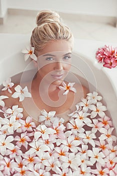 Spa Relax. Blonde enjoying bath with plumeria tropical flowers. Health And Beauty. Closeup Beautiful Sexy Girl Bathing With Petals