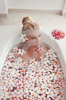 Spa Relax. Blonde enjoying bath with plumeria tropical flowers. Health And Beauty. Closeup Beautiful Sexy Girl Bathing With Petals