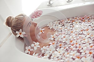 Spa Relax. Blonde enjoying bath with plumeria tropical flowers. Health And Beauty. Closeup Beautiful Sexy Girl Bathing With Petals