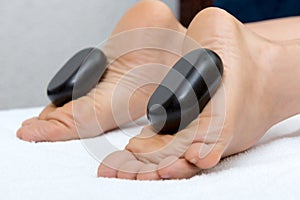 Woman lying on stomach, female masseuse doing legs and feet massage with hot stones