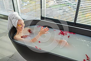 Spa relaxation. Woman lying in bath with red roses petals. Girl relaxing in bathroom at home. Pretty female enjoying