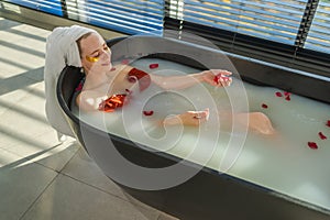 Spa relaxation. Woman lying in bath with red roses petals. Girl relaxing in bathroom at home. Pretty female enjoying