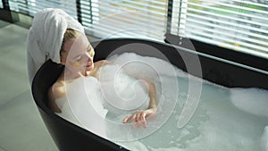 Spa relaxation. Young woman lying in bath with foam bubbles. Girl relaxing in bathroom at home. Pretty female spending