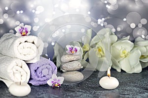 Spa resort therapy composition with massage stones, rolled towels, burning candles, and orchid flowers, abstract lights. Concept