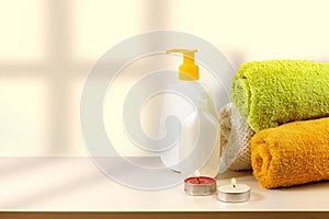 Spa set of massage oil and towels on table with scented candles, bright sunlight with shadows