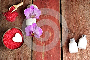 Spa set with red bath salt, orchid and towel flowers, lotion and soap on a wooden background