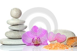 A spa set for Valentines day with stones, an orchid flower and a spatula with salt on a white background