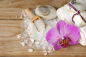 Spa set with white towels, sea salt, wooden spatula and a bright orchid flower, copy space for your text on the left