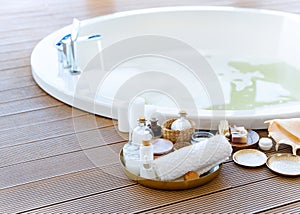 Spa setting in bathroom with round bathtub, cosmetics, sea salt, candles, white towel, soap