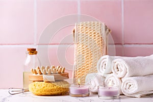 Spa setting with  burning candles, towels, wisk, massager against pink tiled wall.