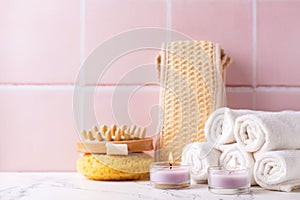 Spa setting with  burning canles, towels, wisk, massager against pink tiled wall.