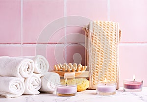 Spa setting with  burning canles, towels, wisk, massager against pink tiled wall.