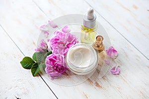 Spa setting with pot of moisturizing cream beautiful pink roses and rose oil on white background