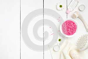 Spa setting with sea salt in bowl, towel, massage tool, chamomile flowers, candles on woode background, top view. Wellness