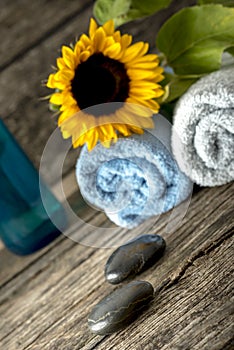 Spa setting with a towels, sunflower on top, massage stones, and