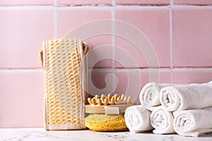Spa setting with towels, wisk, massager against pink tiled wall.