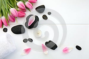 Spa setting with tulips , black stones and towel on white wood background.