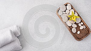 Spa setting with white towels, wooden tray, smooth stones, and a yellow orchid flower on a textured grey background