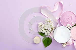 Spa and skin care products cream, and sea bath salt on purple background with spring white lilac blossom.