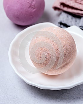 SPA Still Life Background Pink Bath Bomb on White Plate in Shape of Shell Pink and Gray Towels Spa Beauty Concept