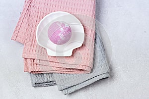 SPA Still Life Background Pink Bath Bomb on White Plate in Shape of Shell Pink and Gray Towels Spa Beauty Concept Top View