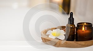 Spa still life with candle, body oil and frangipani flower on wooden plate, home spa and aromatherapy set, clean beauty