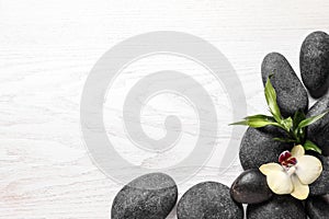 Spa stones, beautiful orchid flower and bamboo sprout on white wooden background, flat lay. Space for text