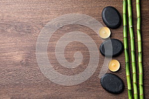 Spa stones, burning candles and bamboo stems on wooden table, flat lay. Space for text