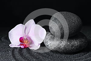 Spa stones and orchid flower on black sand with pattern. Zen concept