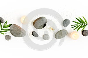 Spa stones, palm leaves, flower white orchid, candle and zen like grey stones on white background. Flat lay, top view