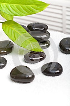 Spa stones on white towel and green leaves