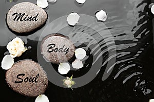 Spa stones with words Mind, Body, Soul and rose petals in water. Zen lifestyle