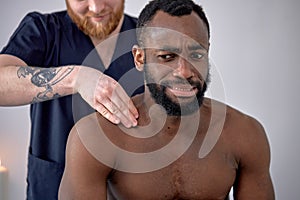Spa therapist making relaxing massage for handsome middle aged black man, rubbing back.